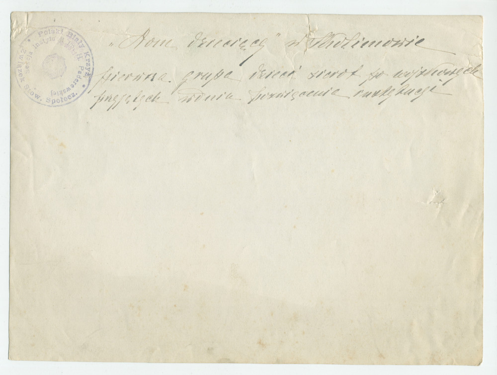 Photographie d'un «premier groupe d'enfants orphelins après les turbulences de la guerre», encadrés par des infirmières et autres adultes – avec légende manuscrite et tampons de la Croix Blanche polonaise au verso